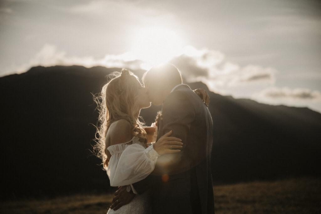 photographie d'un couple de marié dans le massif du vercors au coucher du soleil. Le couple s'embrasse alors que le soleil passe tout juste derrière la montagne créant ainsi une ambiance chaleureuse de photo de mariage